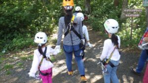 ジップライン体験前に森の中を歩く親子。ヘルメットとハーネスを装着し出発地点へ向かう様子